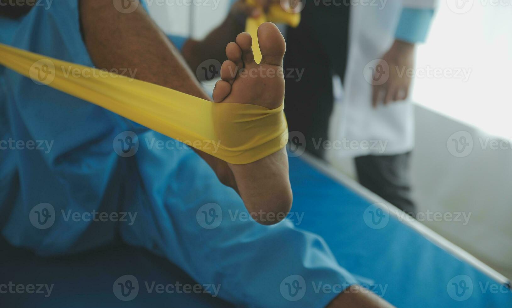 Male patient using elastic band while doing physical exercises for leg muscles at modern clinic, rehabilitation center or hospital. Close up of man's foot. Physiotherapy concept photo
