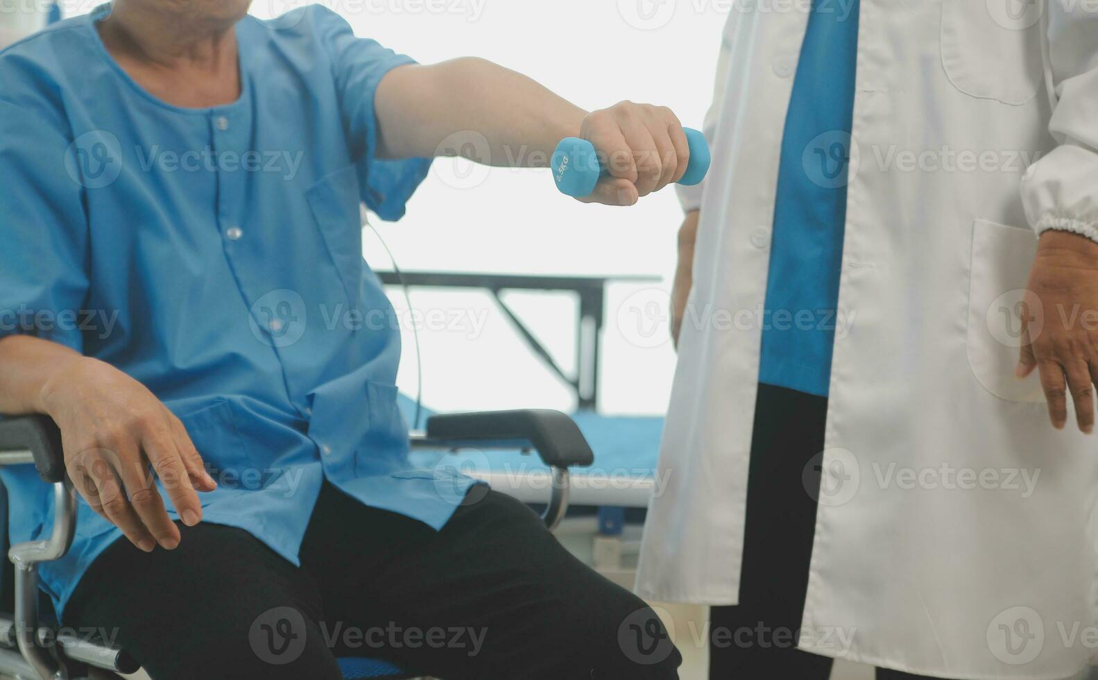 Asian older aged man doing physiotherapist with support from nurse. Senior elderly male sitting on sofa in living room using dumbbells workout exercise for patient with caregiver in nursing care. photo