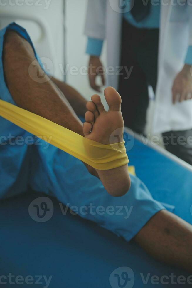 Male patient using elastic band while doing physical exercises for leg muscles at modern clinic, rehabilitation center or hospital. Close up of man's foot. Physiotherapy concept photo