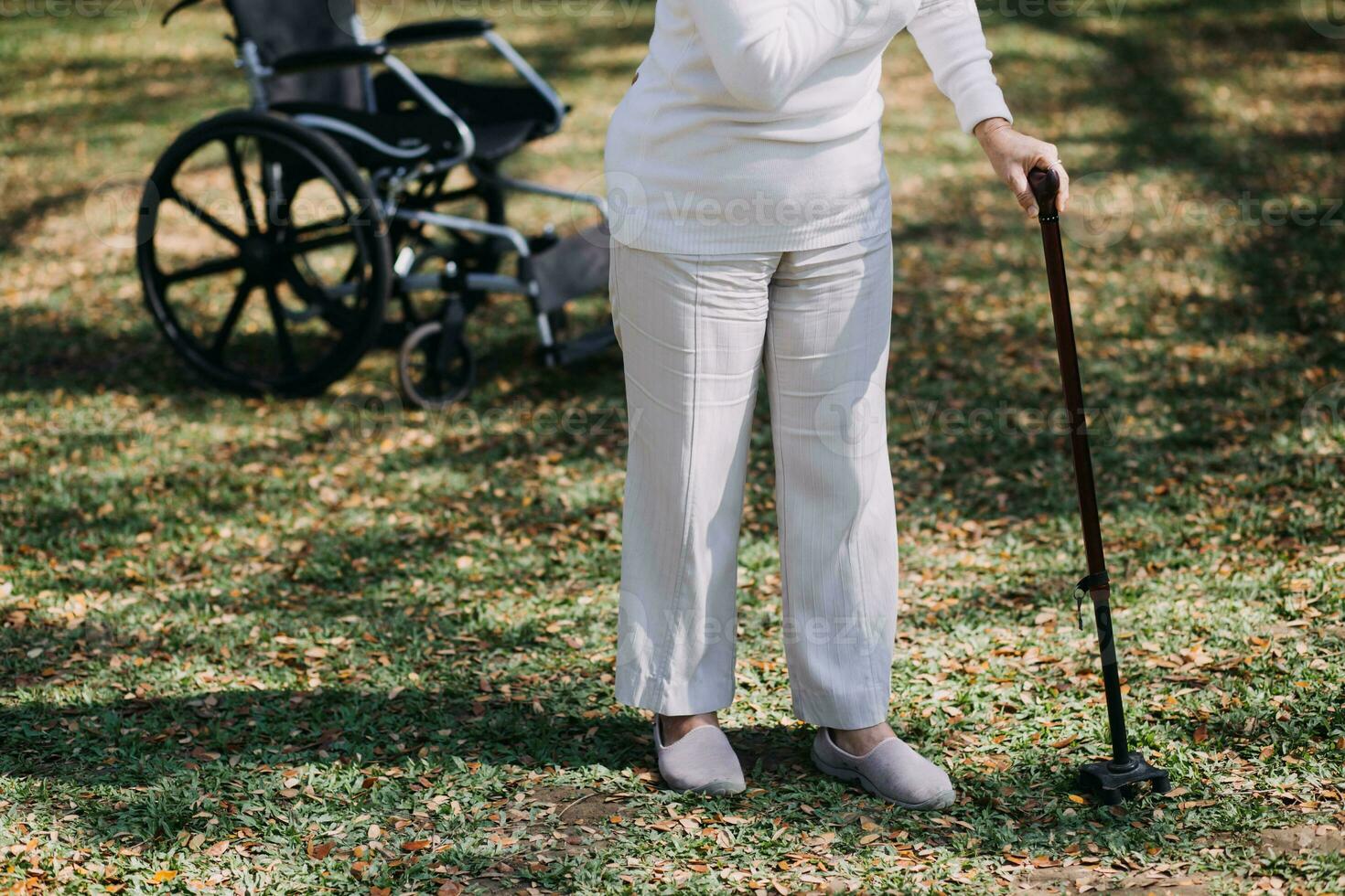 Asian young woman nurse at nursing home take care disabled senior man. Caregiver doctor serve physical therapy for older elderly patient to exercise and practice walking on walker or cane at backyard. photo
