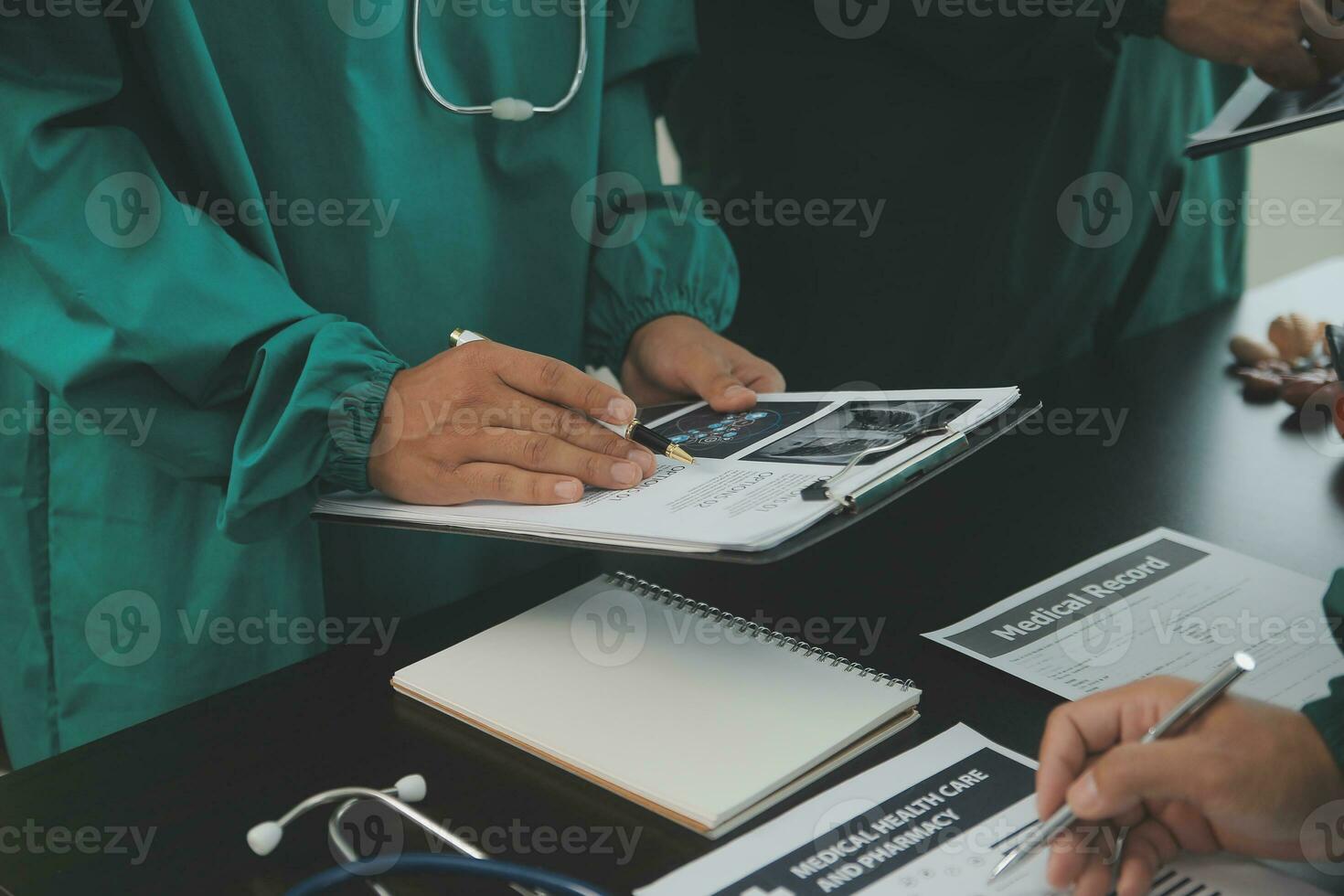 Multiracial team of doctors discussing a patient standing grouped in the foyer looking at a tablet computer, close up view photo