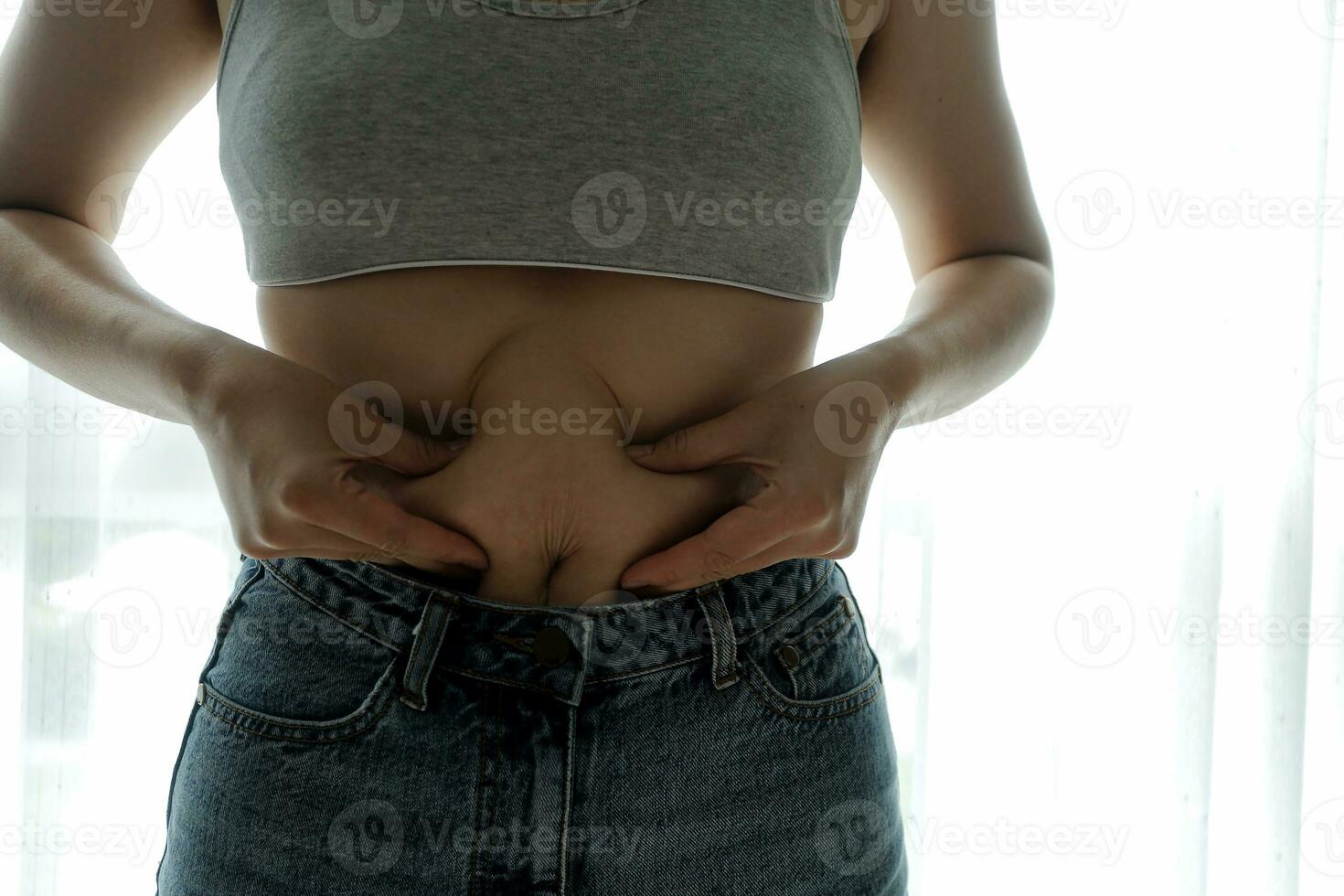 Close up of a belly with scar from c-section and abdominal fat. Women's health. A woman dressed up in sportswear demonstrating her imperfect body after a childbirth with nursery on the background. photo