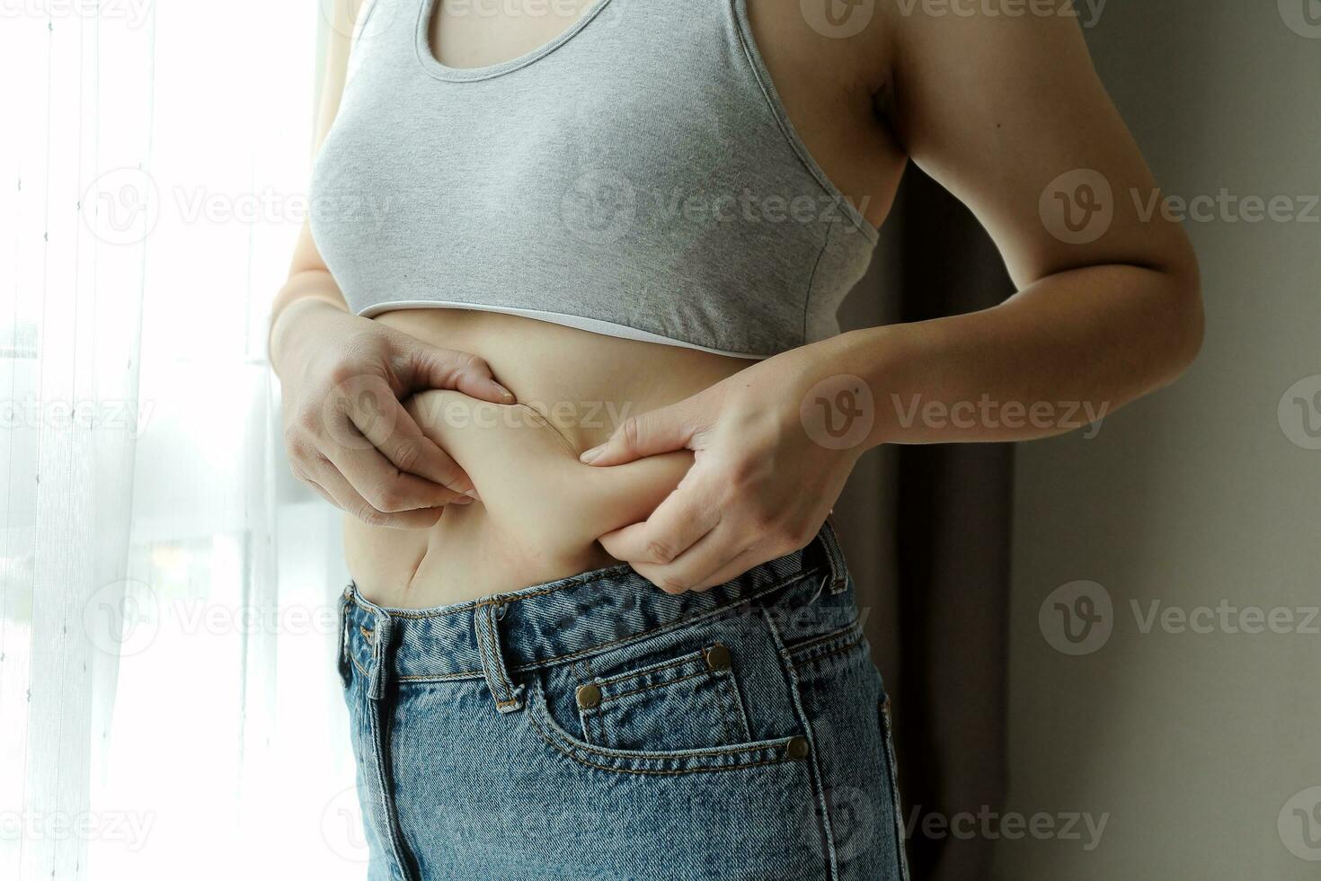 Close up of a belly with scar from c-section and abdominal fat. Women's health. A woman dressed up in sportswear demonstrating her imperfect body after a childbirth with nursery on the background. photo