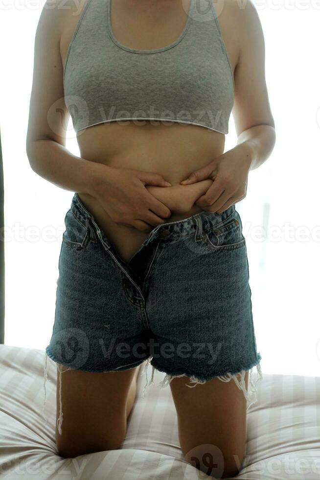 Close up of a belly with scar from c-section and abdominal fat. Women's health. A woman dressed up in sportswear demonstrating her imperfect body after a childbirth with nursery on the background. photo