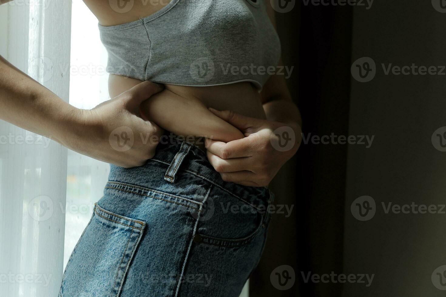 Close up of a belly with scar from c-section and abdominal fat. Women's health. A woman dressed up in sportswear demonstrating her imperfect body after a childbirth with nursery on the background. photo