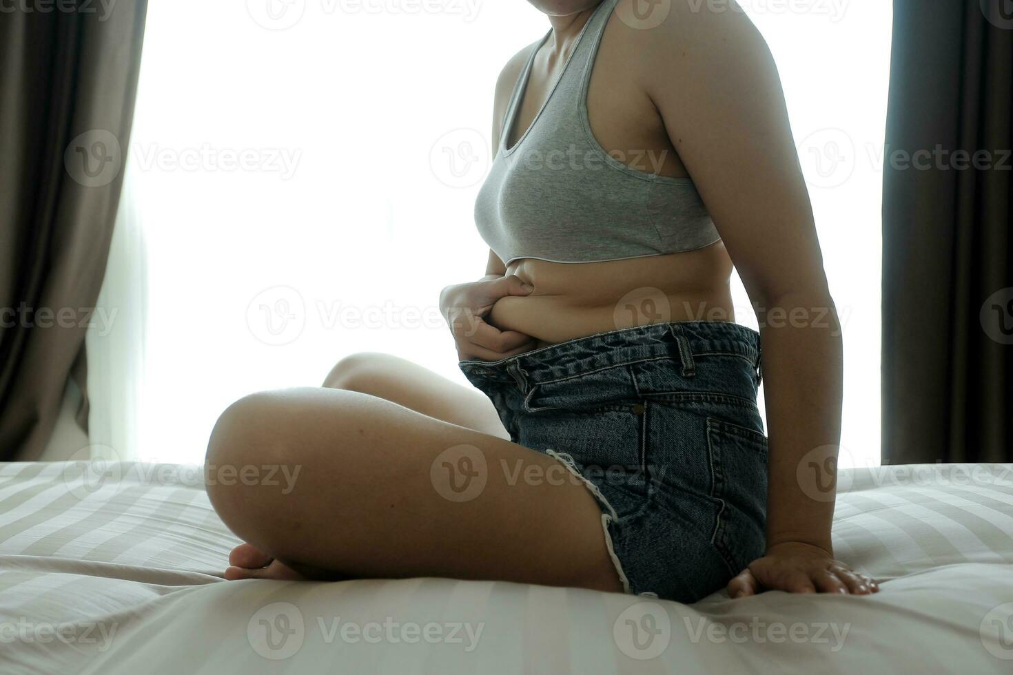 Close up of a belly with scar from c-section and abdominal fat. Women's health. A woman dressed up in sportswear demonstrating her imperfect body after a childbirth with nursery on the background. photo