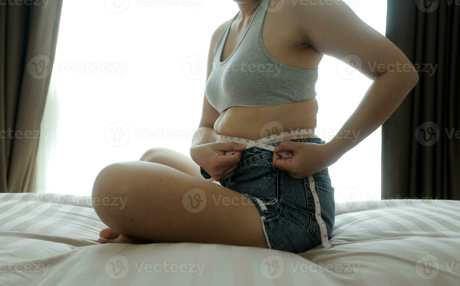 Close up of a belly with scar from c-section and abdominal fat. Women's health. A woman dressed up in sportswear demonstrating her imperfect body after a childbirth with nursery on the background. photo