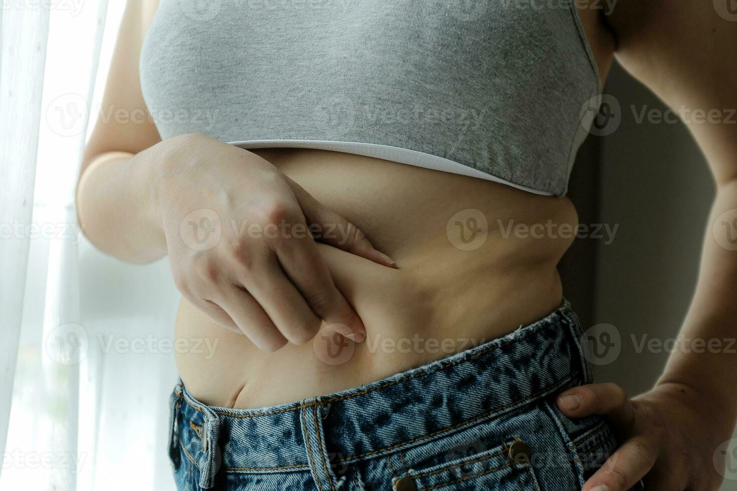 Close up of a belly with scar from c-section and abdominal fat. Women's health. A woman dressed up in sportswear demonstrating her imperfect body after a childbirth with nursery on the background. photo