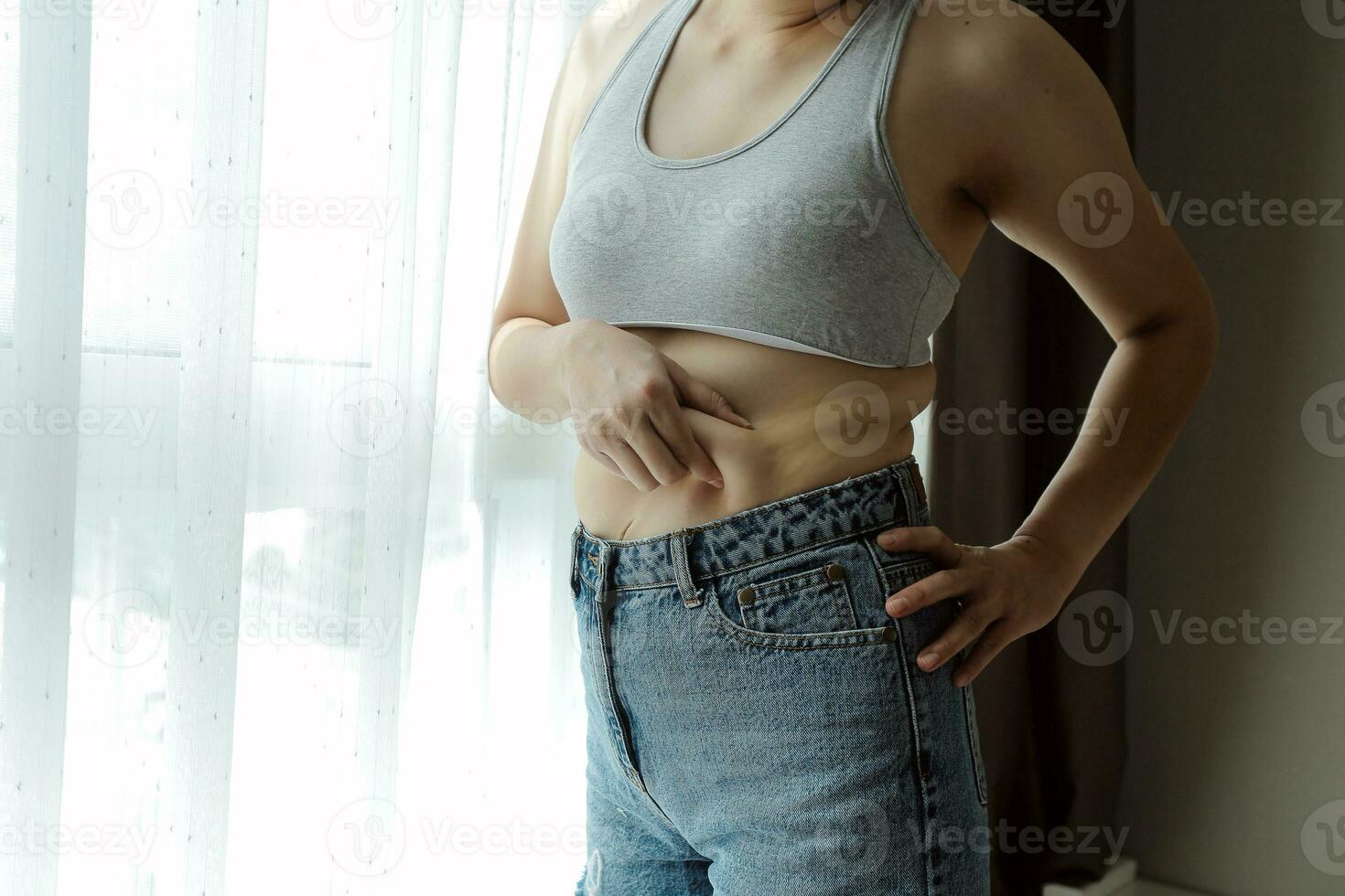 Close up of a belly with scar from c-section and abdominal fat. Women's health. A woman dressed up in sportswear demonstrating her imperfect body after a childbirth with nursery on the background. photo