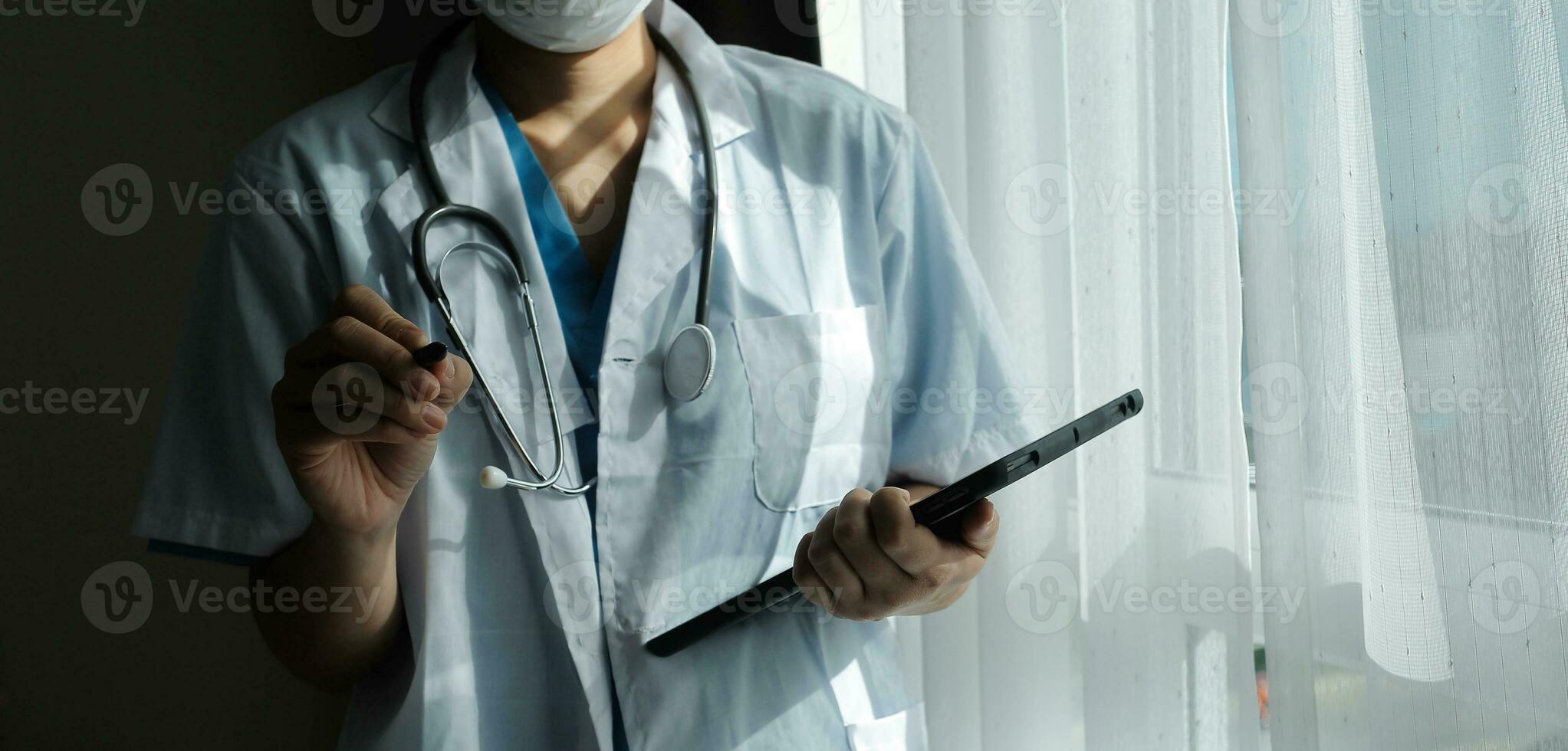 Female Doctor Wearing Scrubs In Hospital Corridor Using Digital Tablet photo