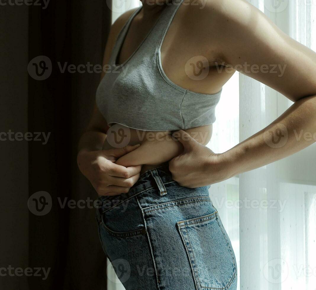 Close up of a belly with scar from c-section and abdominal fat. Women's health. A woman dressed up in sportswear demonstrating her imperfect body after a childbirth with nursery on the background. photo