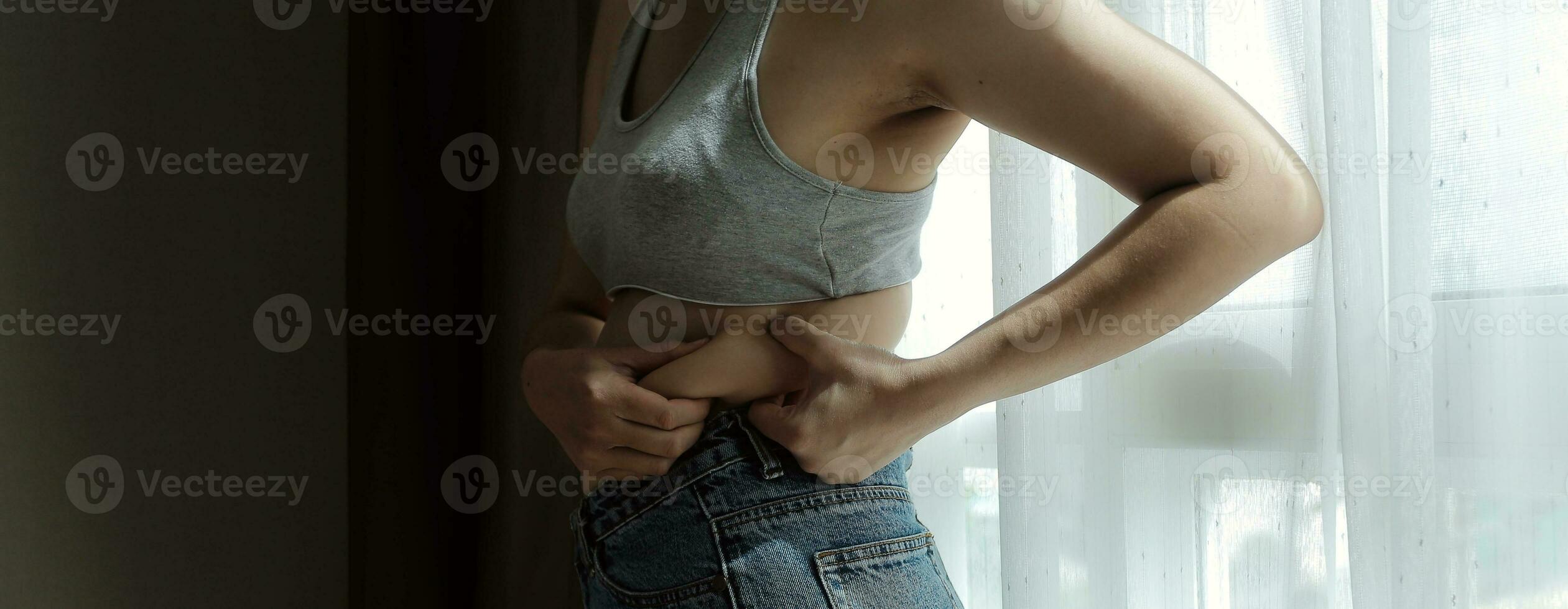 Close up of a belly with scar from c-section and abdominal fat. Women's health. A woman dressed up in sportswear demonstrating her imperfect body after a childbirth with nursery on the background. photo