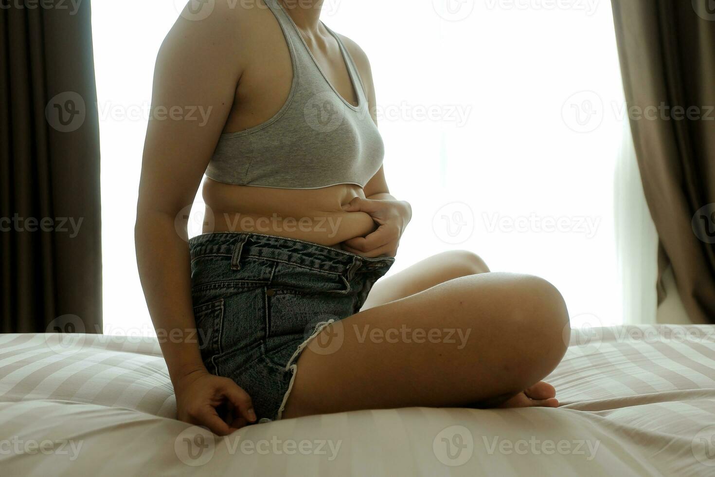 Close up of a belly with scar from c-section and abdominal fat. Women's health. A woman dressed up in sportswear demonstrating her imperfect body after a childbirth with nursery on the background. photo