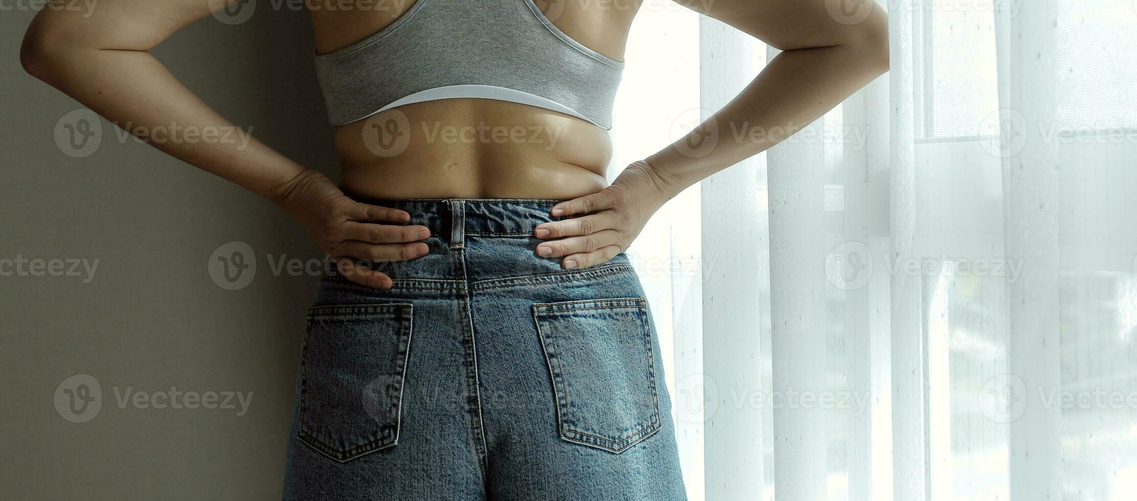 Close up of a belly with scar from c-section and abdominal fat. Women's health. A woman dressed up in sportswear demonstrating her imperfect body after a childbirth with nursery on the background. photo
