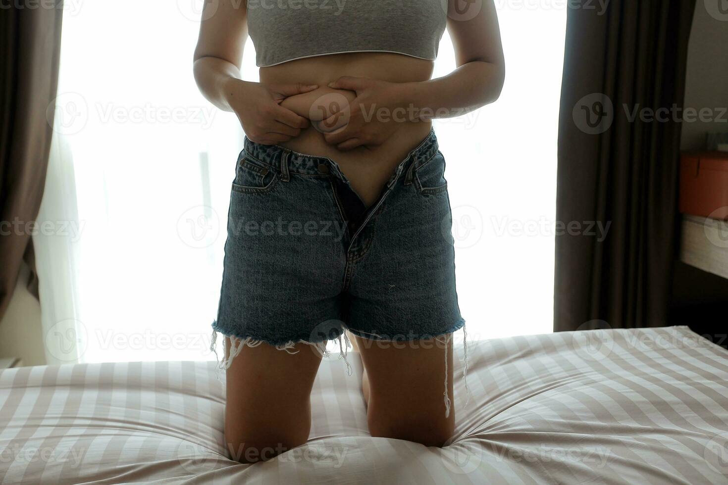 Close up of a belly with scar from c-section and abdominal fat. Women's health. A woman dressed up in sportswear demonstrating her imperfect body after a childbirth with nursery on the background. photo