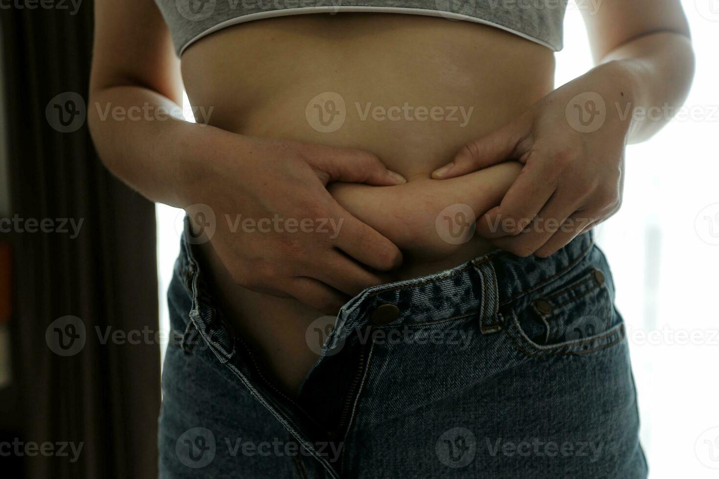 Close up of a belly with scar from c-section and abdominal fat. Women's health. A woman dressed up in sportswear demonstrating her imperfect body after a childbirth with nursery on the background. photo