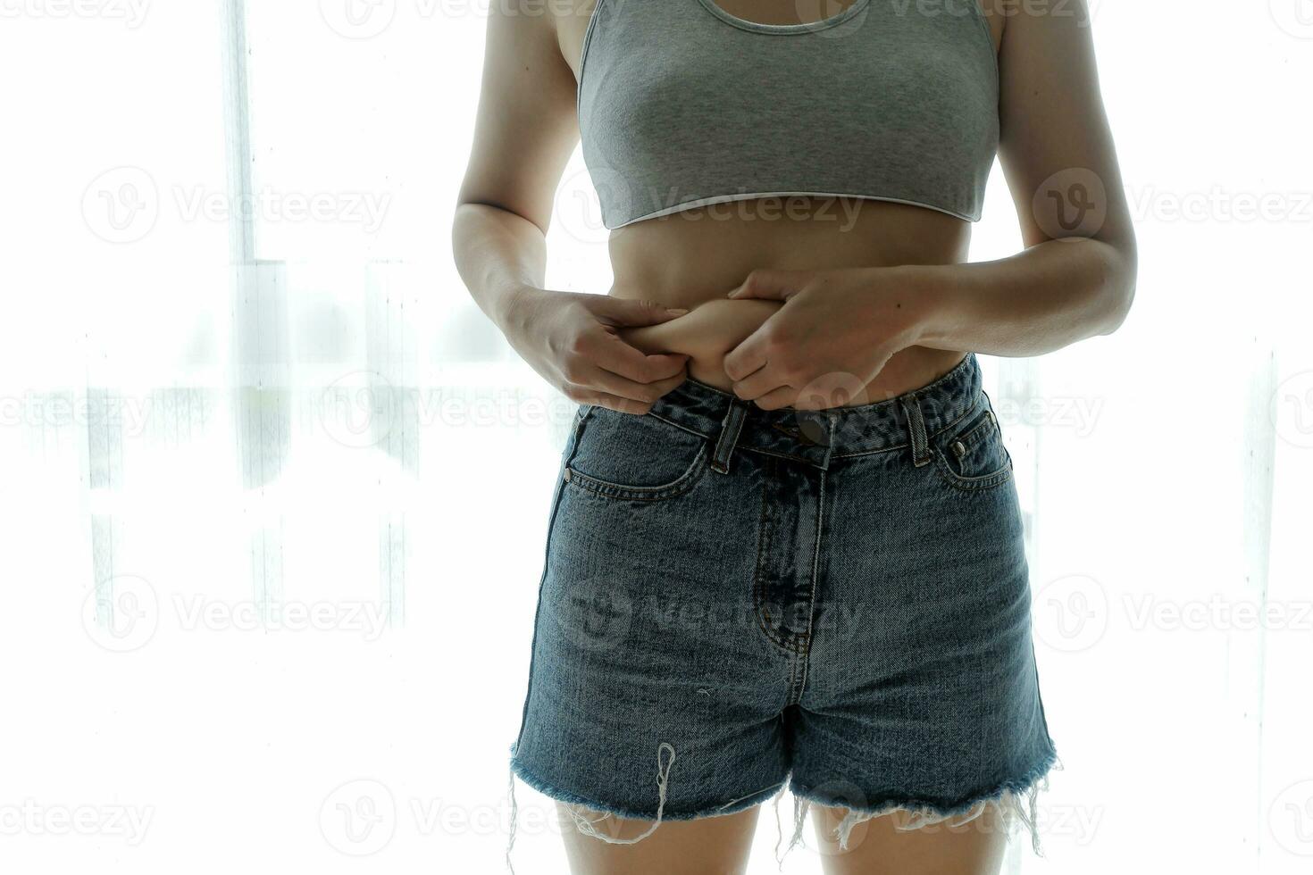 Close up of a belly with scar from c-section and abdominal fat. Women's health. A woman dressed up in sportswear demonstrating her imperfect body after a childbirth with nursery on the background. photo