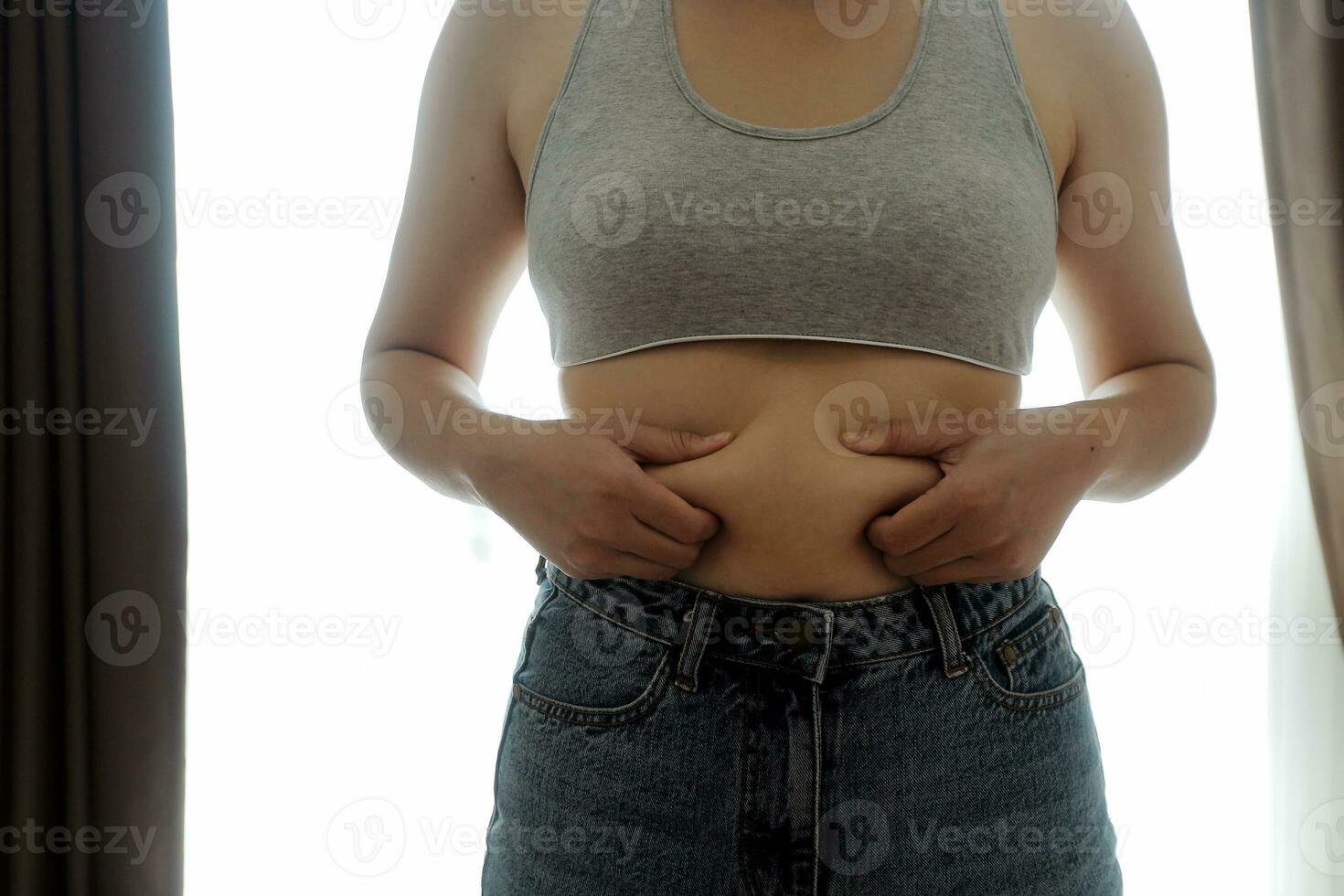 Close up of a belly with scar from c-section and abdominal fat. Women's health. A woman dressed up in sportswear demonstrating her imperfect body after a childbirth with nursery on the background. photo