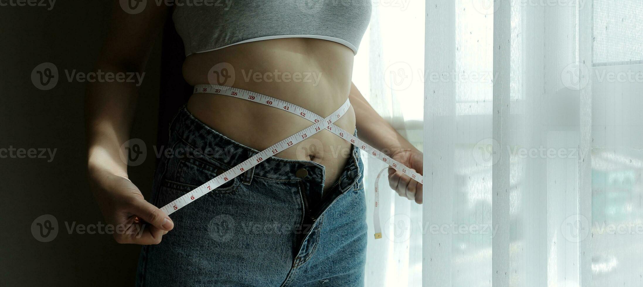 Close up of a belly with scar from c-section and abdominal fat. Women's health. A woman dressed up in sportswear demonstrating her imperfect body after a childbirth with nursery on the background. photo