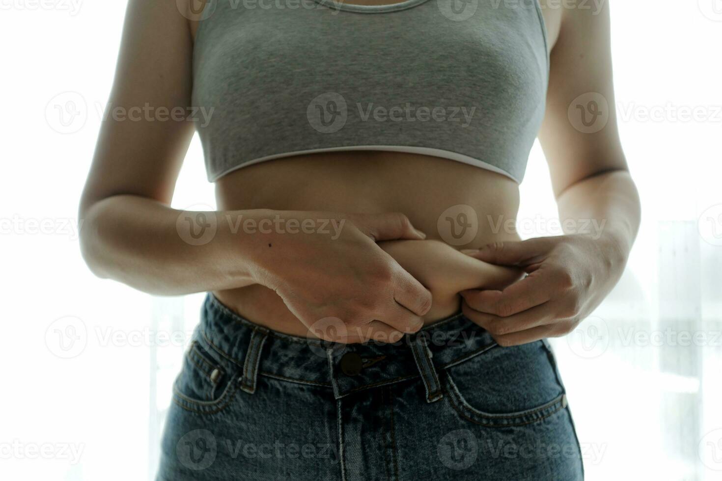 Close up of a belly with scar from c-section and abdominal fat. Women's health. A woman dressed up in sportswear demonstrating her imperfect body after a childbirth with nursery on the background. photo