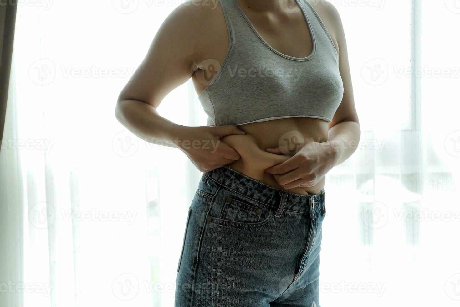 Close up of a belly with scar from c-section and abdominal fat. Women's health. A woman dressed up in sportswear demonstrating her imperfect body after a childbirth with nursery on the background. photo