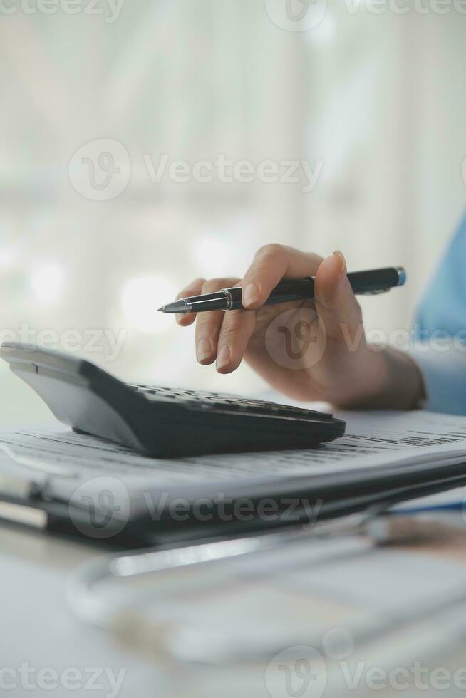Doctor or physician using calculator and work on laptop computer with medical stethoscope on the desk at clinic or hospital. Medical healthcare costs ,fees and revenue concept. photo