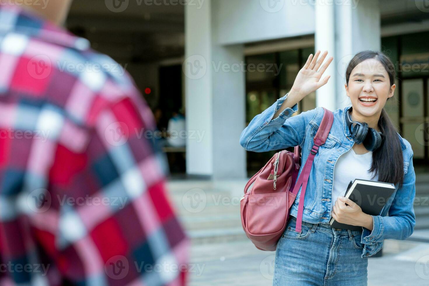 Beautiful student woman with backpack and books outdoor is greeting friends. Smile girl happy carrying a lot of book in college campus. Portrait female on international Asia University. Education photo