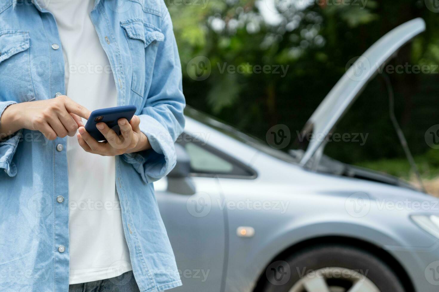 breakdown, broken car, repair. Woman uses mobile phone check insurance premiums through application due to car accident . Find garage to get car fixed during country tour, waiting for help, emergency. photo