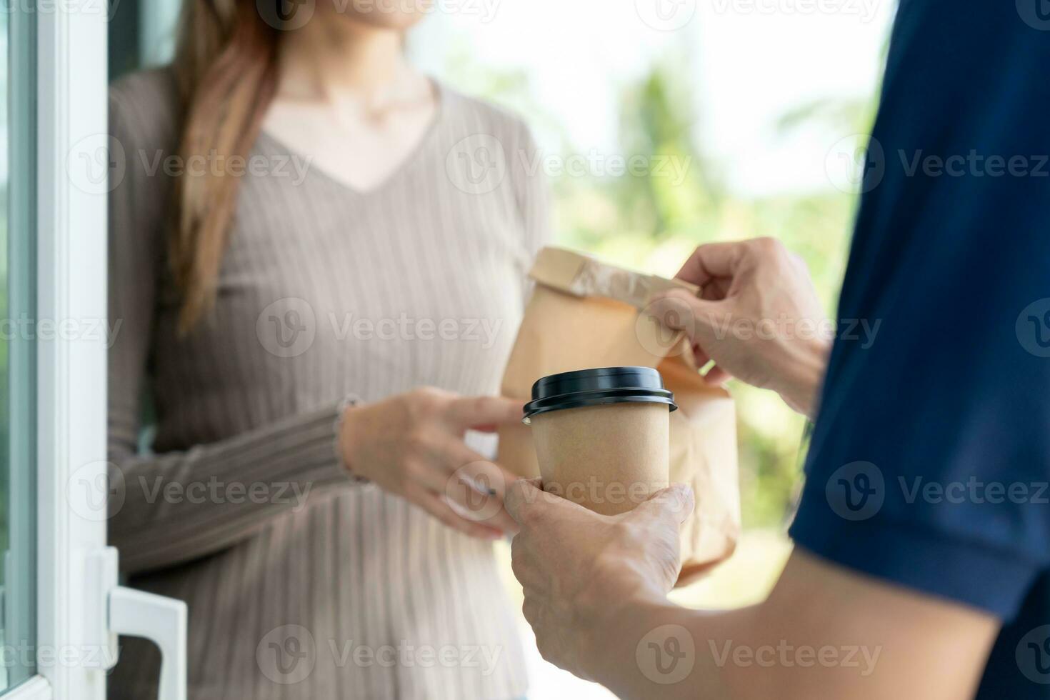 Happy smiling Asian woman receives paper box parcel of food from courier front house. Delivery man send deliver express. online shopping, paper container, takeaway, postman, delivery service, packages photo