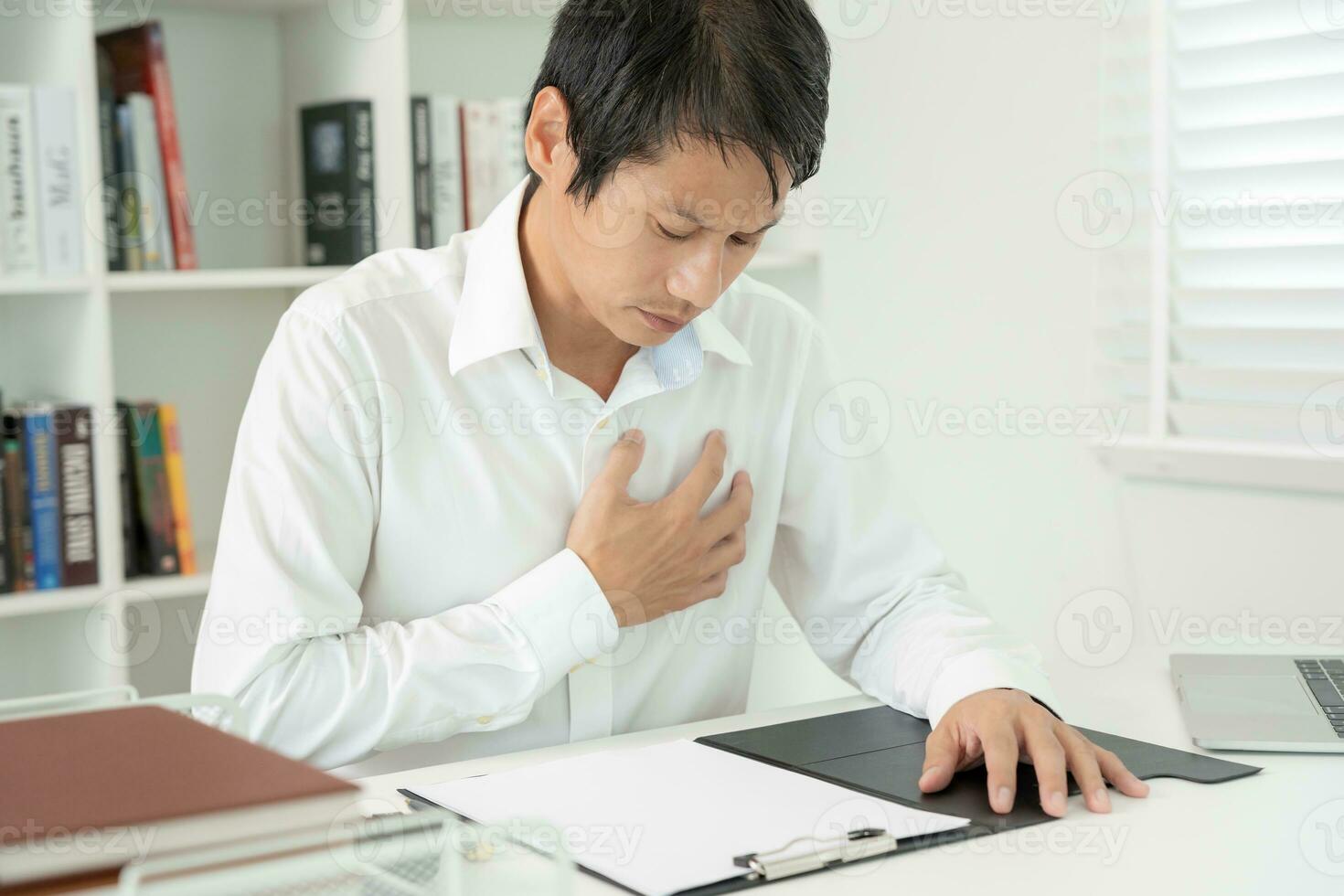 hand hold chest with heart attack symptoms, asian man working hard have chest pain caused by heart disease, leak, dilatation, enlarged coronary heart, press on the chest with a painful expression photo