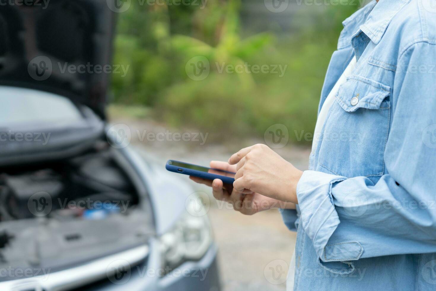 breakdown, broken car, repair. Woman uses mobile phone check insurance premiums through application due to car accident . Find garage to get car fixed during country tour, waiting for help, emergency. photo