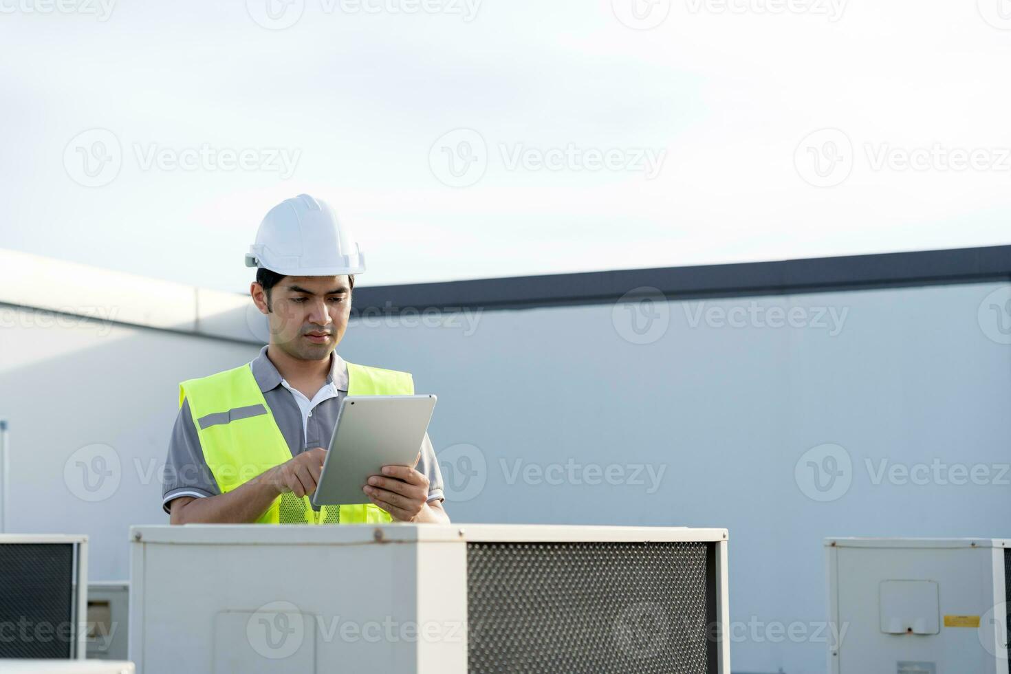 Asian maintenance engineer works on the roof of factory. contractor inspect compressor system and plans installation of air condition systems in construction. technology, online, mobile application. photo