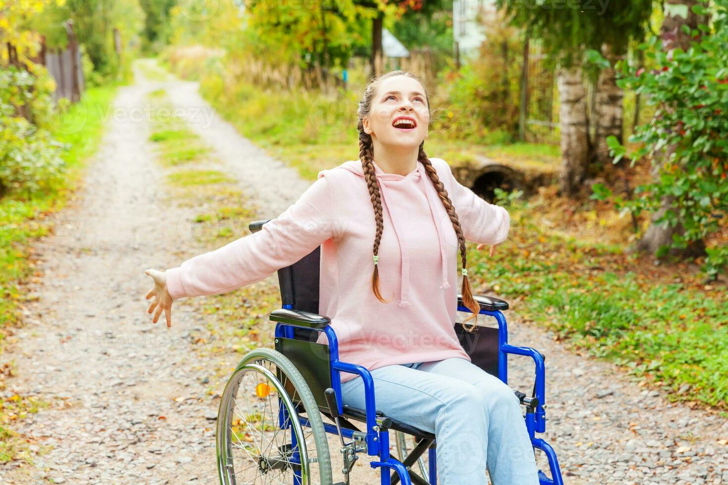 joven discapacitada feliz en silla de ruedas en la carretera en el parque del hospital disfrutando de la libertad. niña paralizada en silla inválida para personas discapacitadas al aire libre en la naturaleza. concepto de rehabilitación. foto