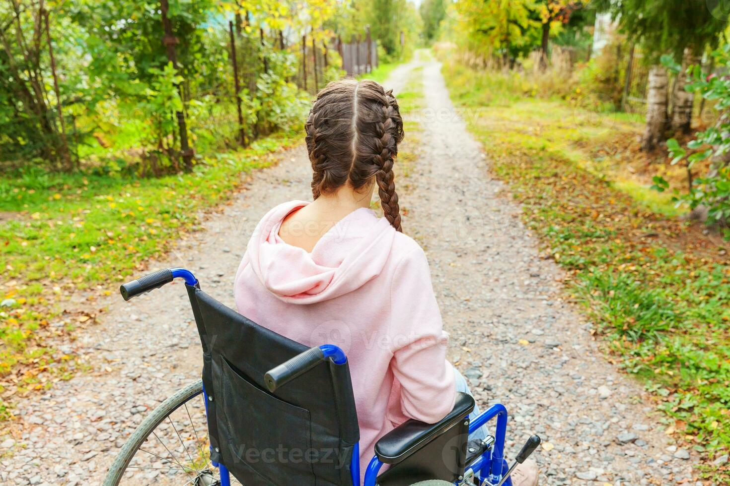 Young happy handicap woman in wheelchair on road in hospital park waiting for patient services. Paralyzed girl in invalid chair for disabled people outdoor in nature. Rehabilitation concept. photo
