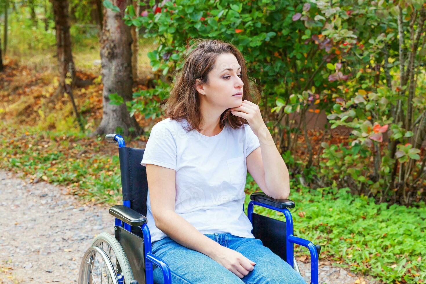 Young happy handicap woman in wheelchair on road in hospital park waiting for patient services. Paralyzed girl in invalid chair for disabled people outdoor in nature. Rehabilitation concept. photo