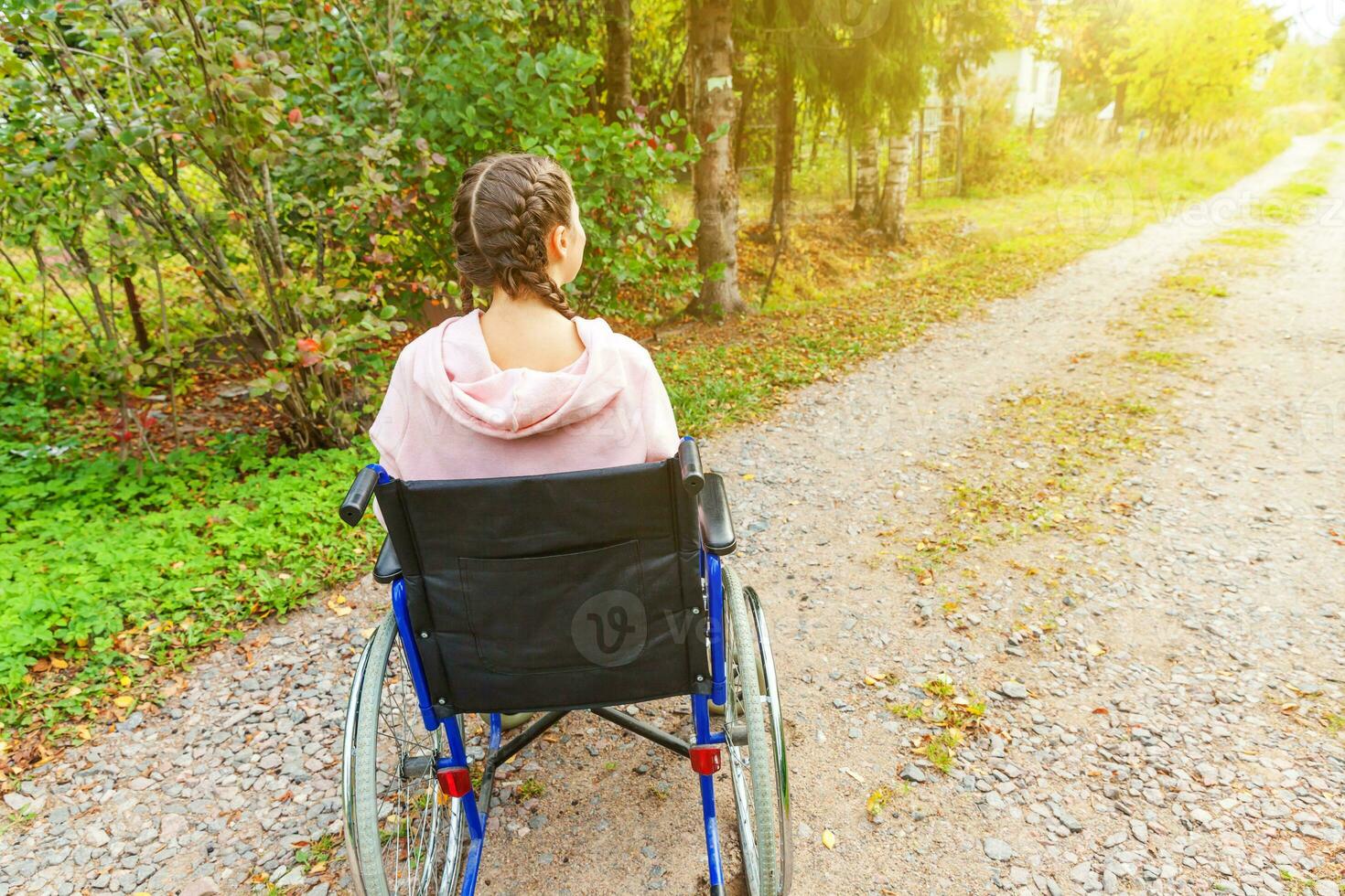 Young happy handicap woman in wheelchair on road in hospital park waiting for patient services. Paralyzed girl in invalid chair for disabled people outdoor in nature. Rehabilitation concept. photo