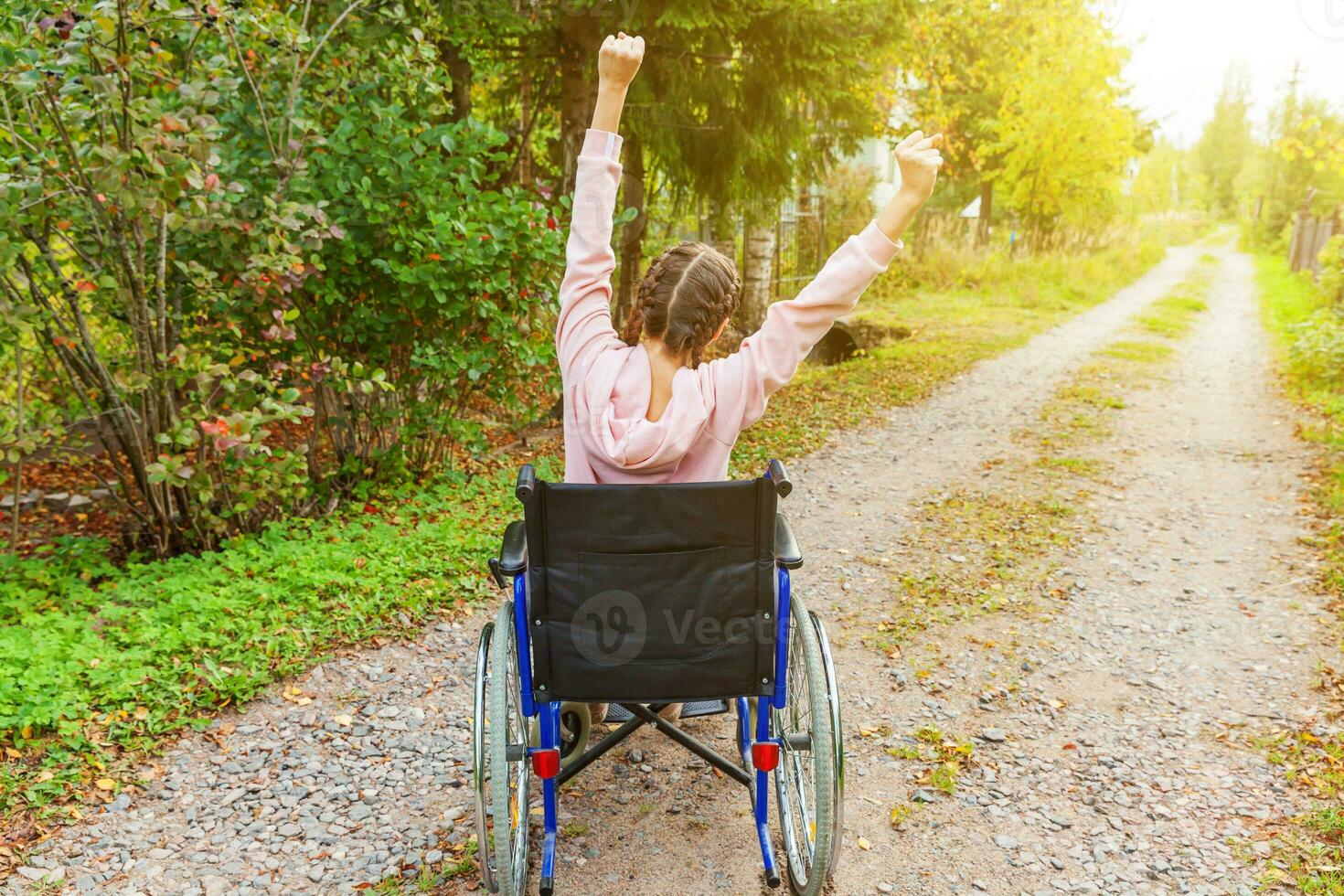 joven discapacitada feliz en silla de ruedas en la carretera en el parque del hospital disfrutando de la libertad. niña paralizada en silla inválida para personas discapacitadas al aire libre en la naturaleza. concepto de rehabilitación. foto