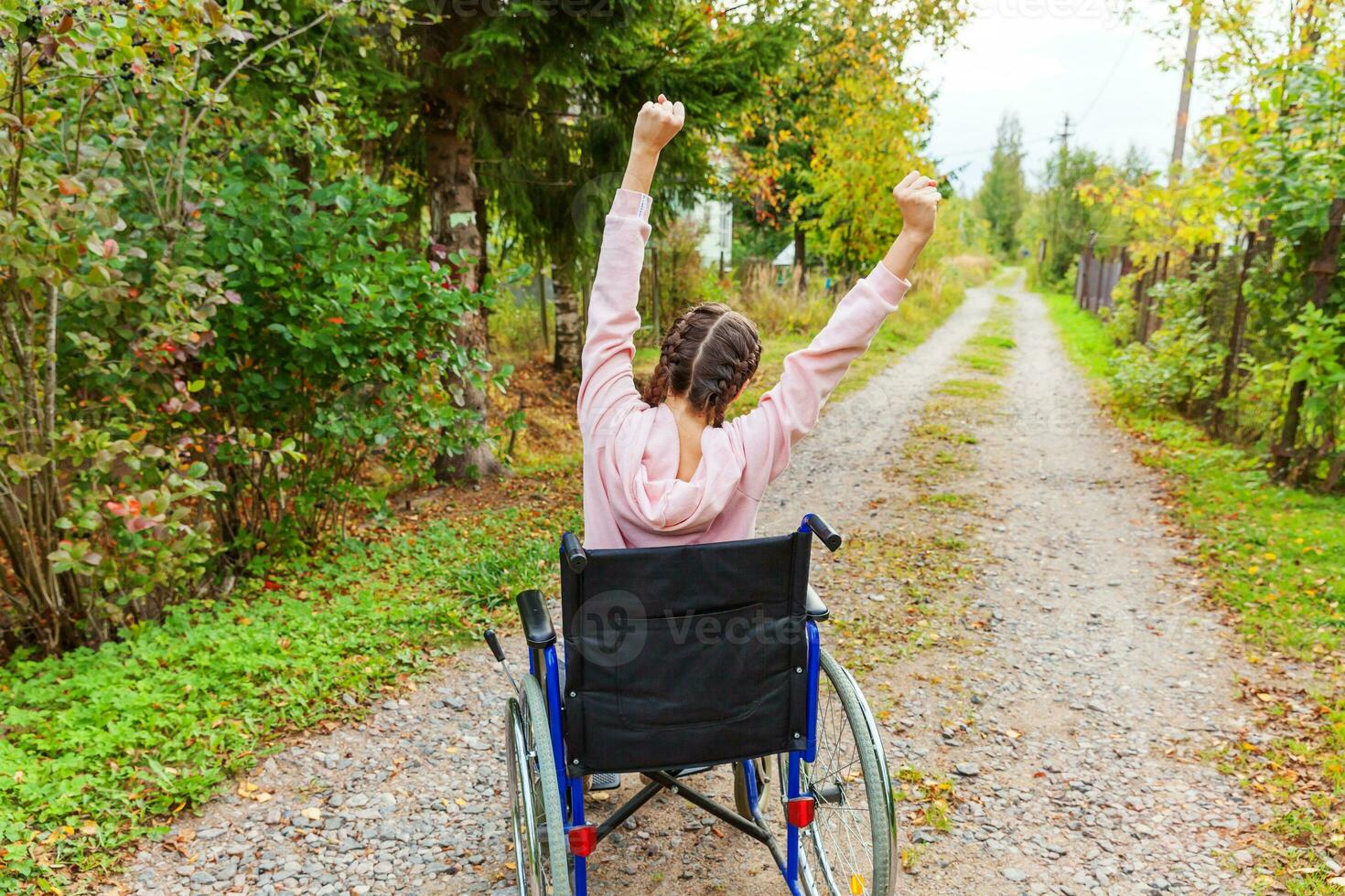 joven discapacitada feliz en silla de ruedas en la carretera en el parque del hospital disfrutando de la libertad. niña paralizada en silla inválida para personas discapacitadas al aire libre en la naturaleza. concepto de rehabilitación. foto