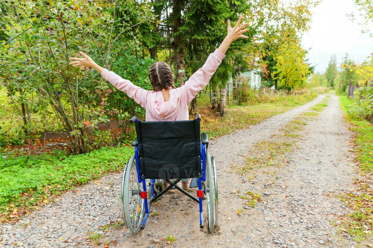 Young happy handicap woman in wheelchair on road in hospital park enjoying freedom. Paralyzed girl in invalid chair for disabled people outdoor in nature. Rehabilitation concept. photo
