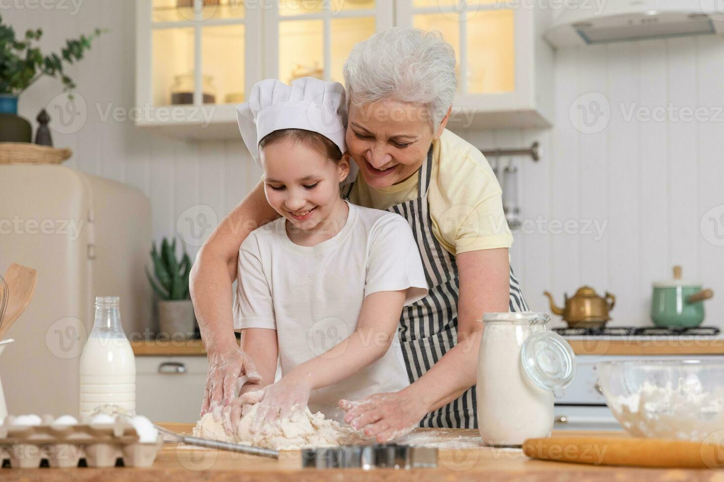 Happy family in kitchen. Grandmother and granddaughter child cook in kitchen together. Grandma teaching kid girl knead dough bake cookies. Household teamwork helping family generations concept. photo