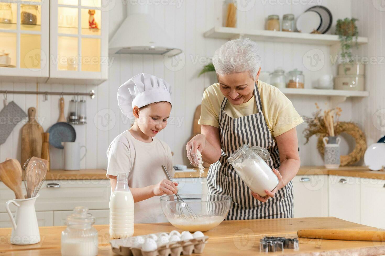 Happy family in kitchen. Grandmother and granddaughter child cook in kitchen together. Grandma teaching kid girl knead dough bake cookies. Household teamwork helping family generations concept. photo