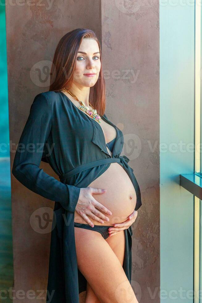 Pregnancy woman standing near window at home and smiles photo