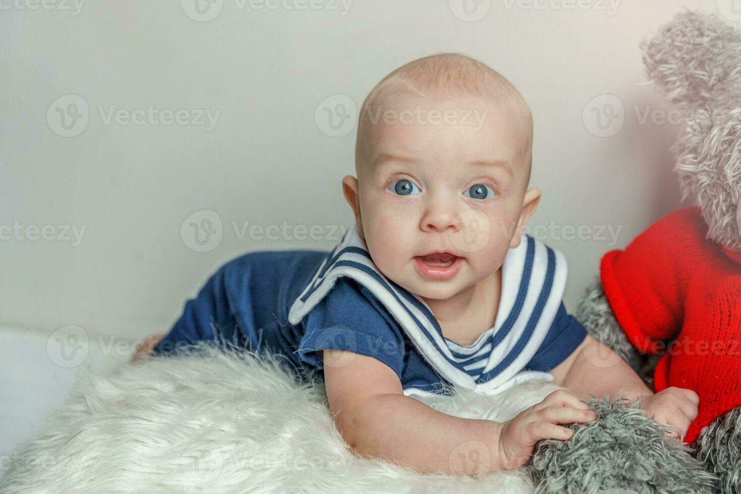 Infant baby boy lies on pillow with teddy bear toy on white bedroom background photo