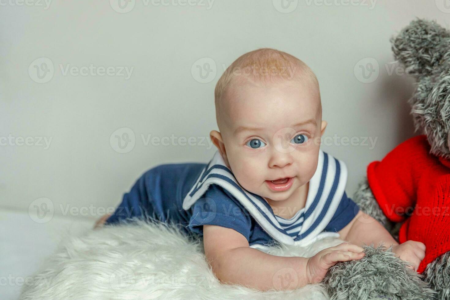 Infant baby boy lies on pillow with teddy bear toy on white bedroom background photo