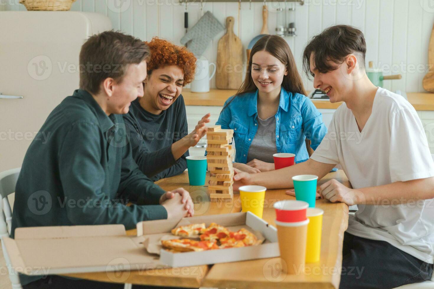 Home party. Friends spending time together playing in board game crash wooden tower at home. Happy diverse group having fun together indoor. Mixed race young buddies best friends enjoying weekend. photo