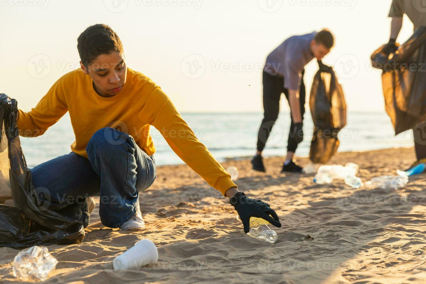 Earth day. Volunteers activists collects garbage cleaning of beach coastal zone. Woman and mans puts plastic trash in garbage bag on ocean shore. Environmental conservation coastal zone cleaning. photo