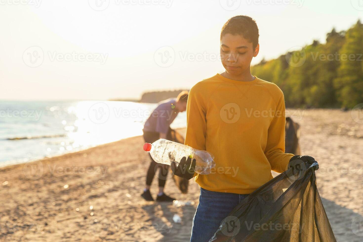 Earth day. Volunteers activists collects garbage cleaning of beach coastal zone. Woman puts plastic bottle trash in garbage bag on ocean shore. Environmental conservation coastal zone cleaning. photo