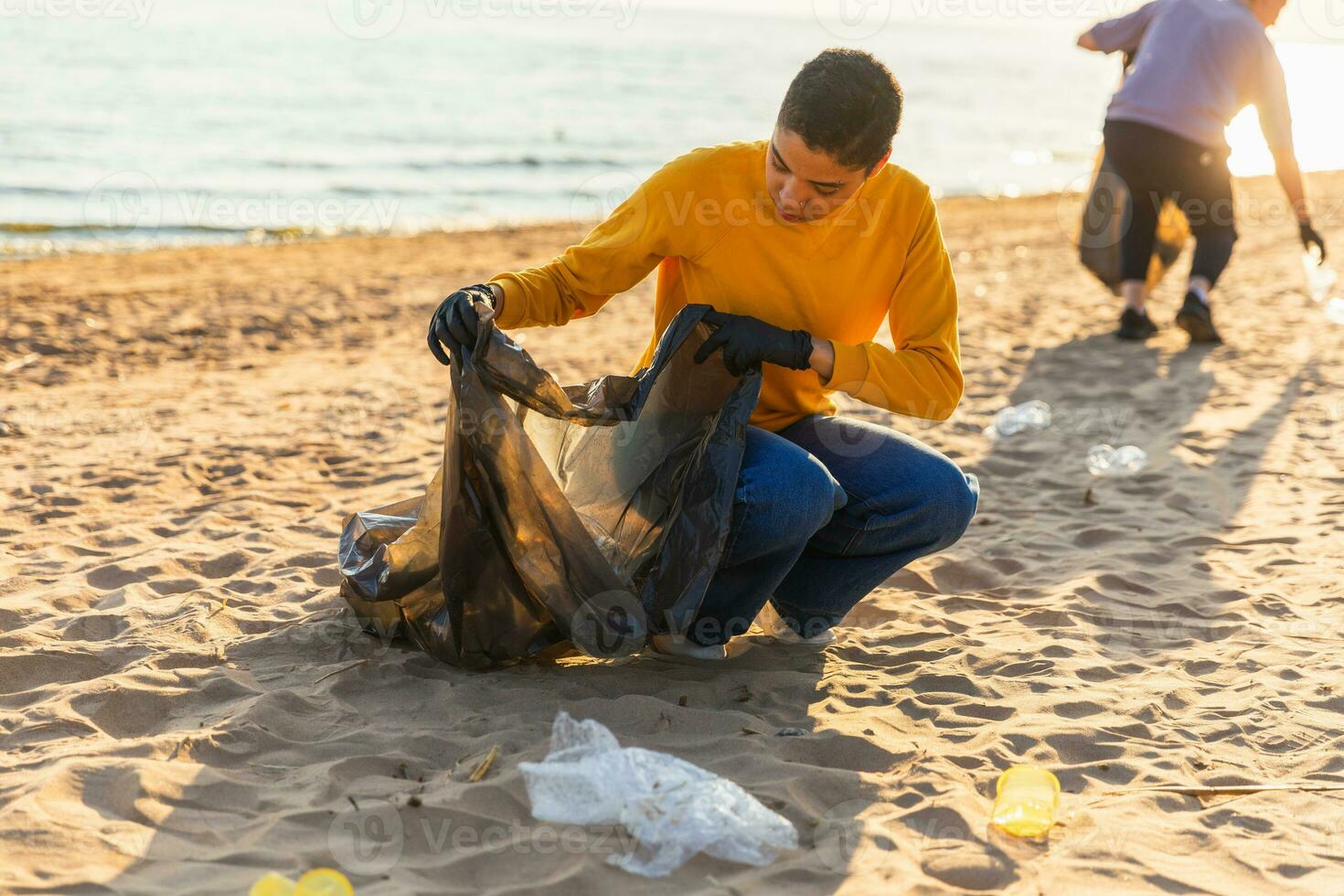 tierra día. voluntarios activistas recoge basura limpieza de playa costero zona. mujer y mans pone el plastico basura en basura bolso en Oceano costa. ambiental conservación costero zona limpieza. foto