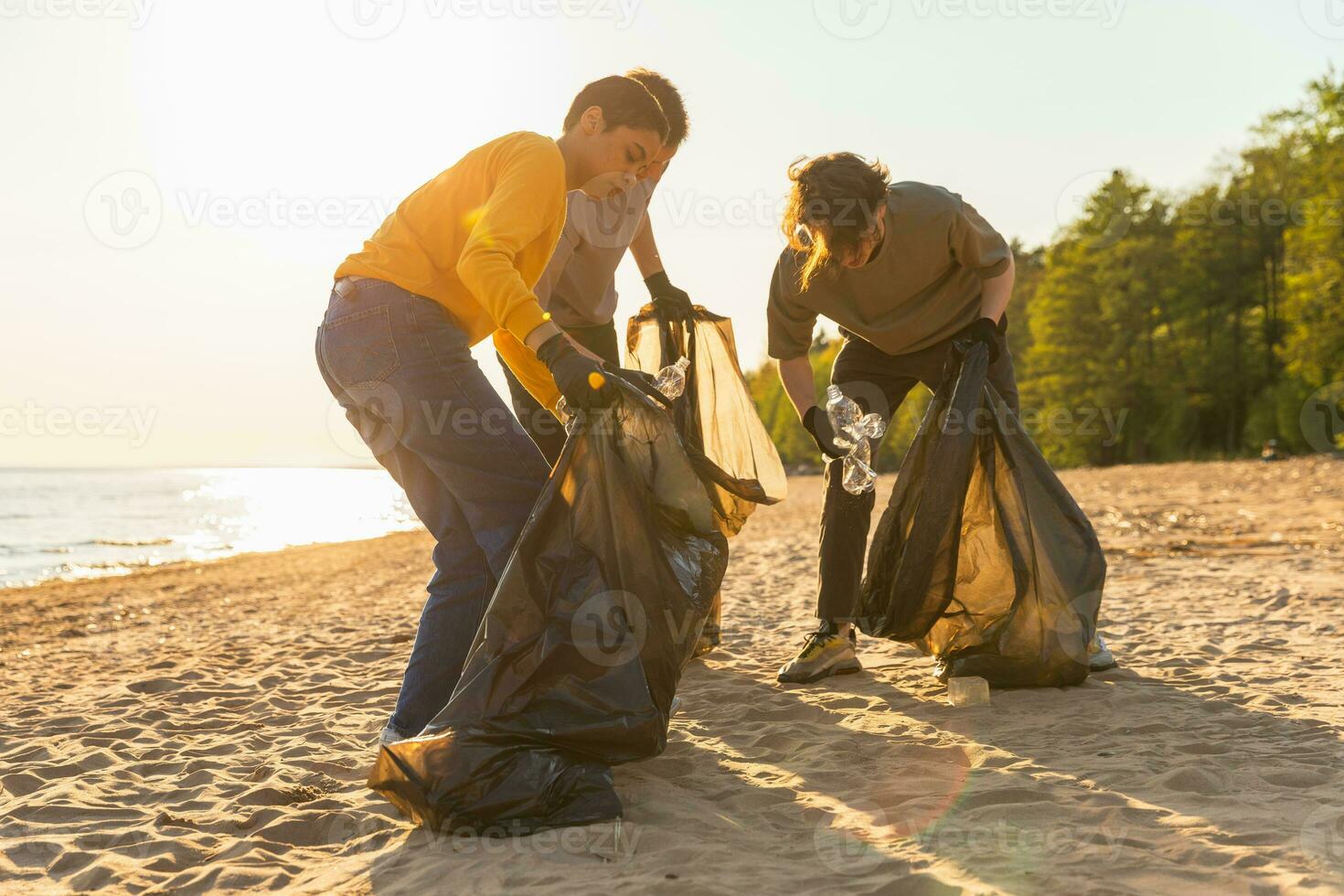 Earth day. Volunteers activists team collects garbage cleaning of beach coastal zone. Group of people puts plastic trash in garbage bags on ocean shore. Environmental conservation. photo