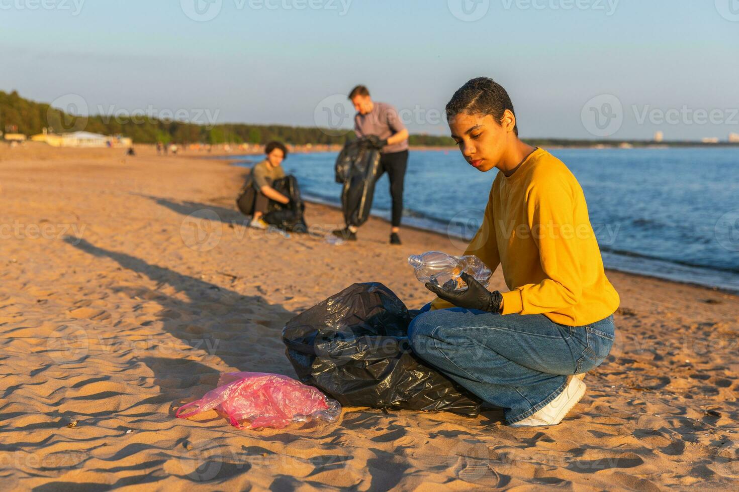 Earth day. Volunteers activists collects garbage cleaning of beach coastal zone. Woman and mans puts plastic trash in garbage bag on ocean shore. Environmental conservation coastal zone cleaning. photo